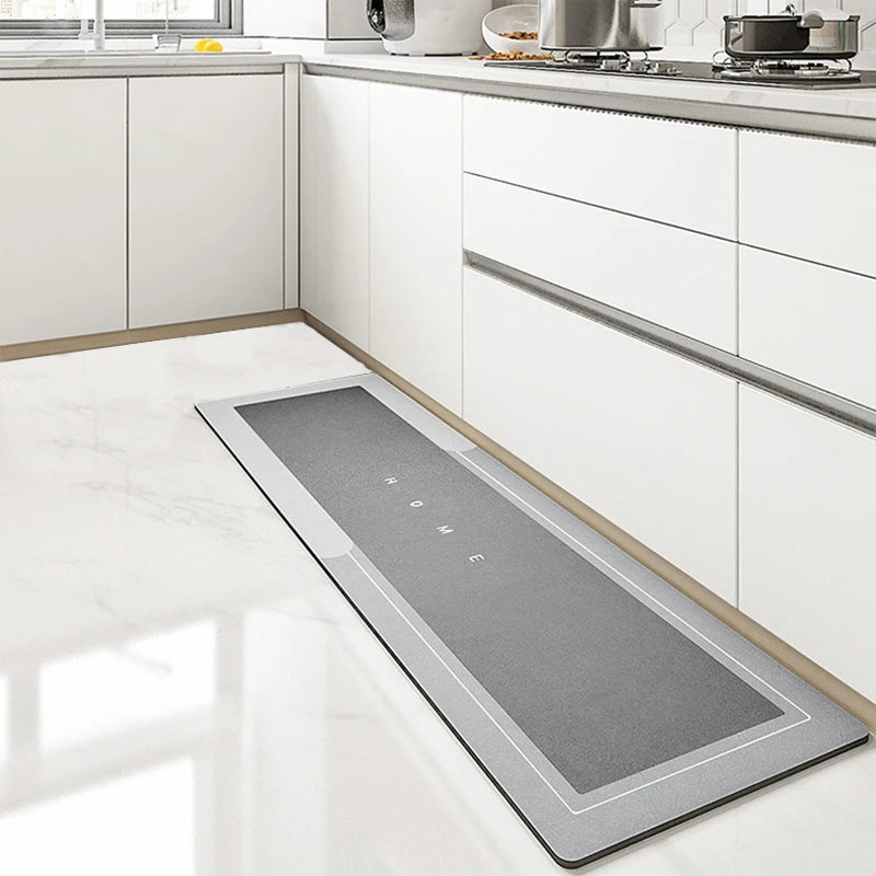 A rectangular gray non-slip floor mat is placed on a white marble kitchen floor next to white cabinetry.