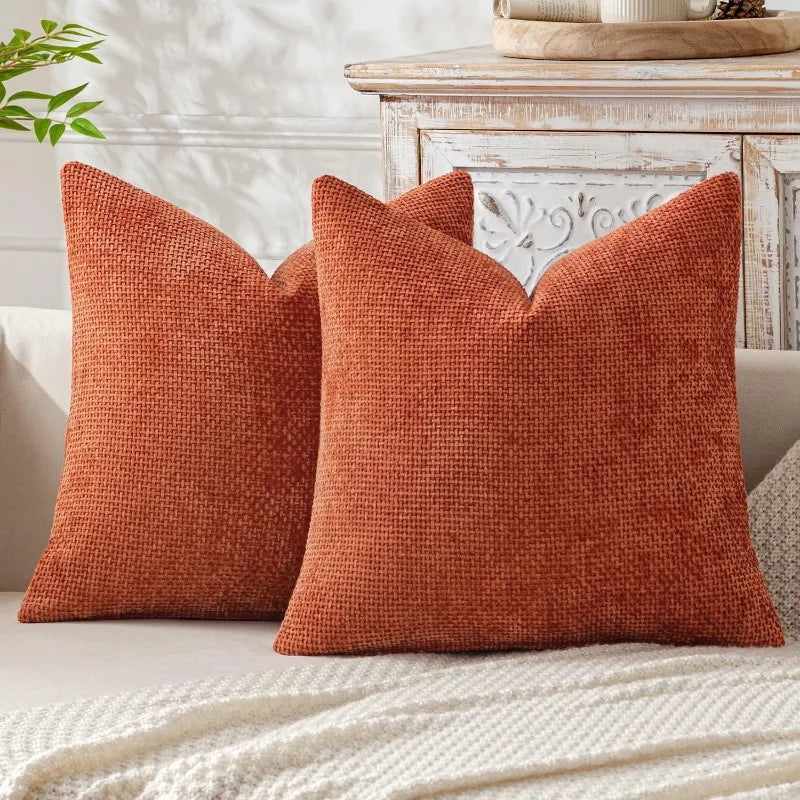 A square, textured burnt orange chenille pillow cover with a subtle scalloped edge resting on a light-colored sofa.