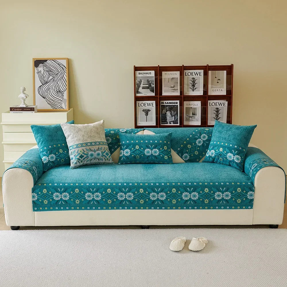 A teal chenille sofa cover featuring a white floral pattern displayed on a light beige wall.