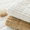 A beige corduroy sofa armrest cover is shown next to a white ribbed textile and some white pom-poms.