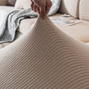 A hand is touching a beige, ribbed seat cushion cover fabric on a sofa.