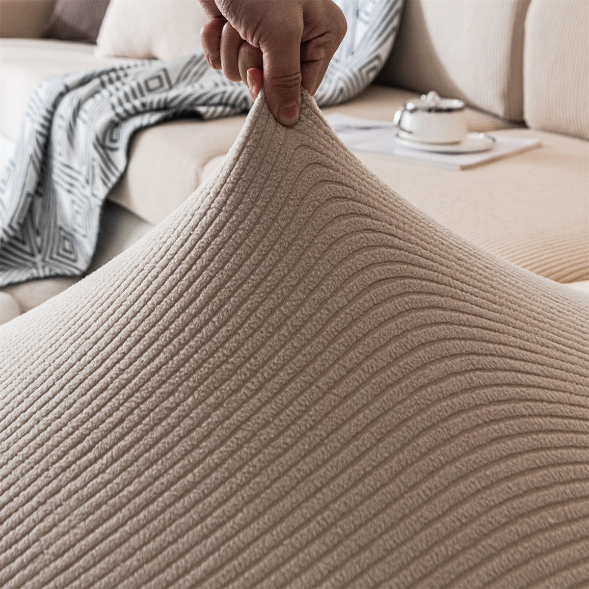 A hand is touching a beige, ribbed seat cushion cover fabric on a sofa.
