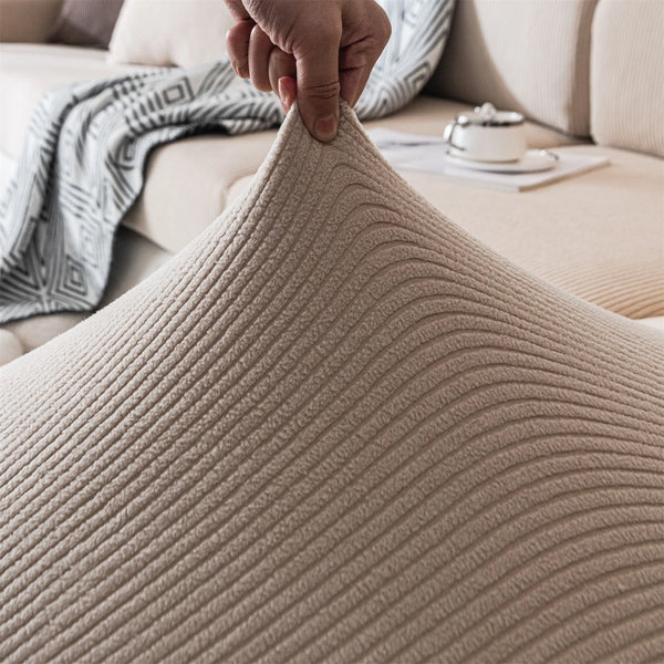 A hand is touching a beige, ribbed seat cushion cover fabric on a sofa.