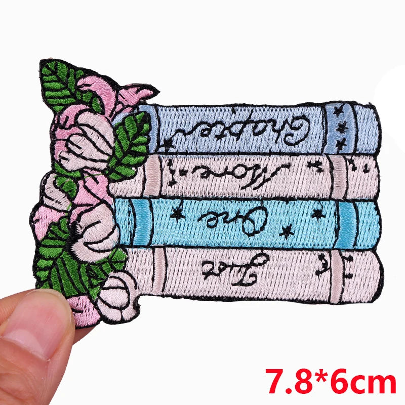 A set of embroidered letter iron-on patches featuring floral designs and text on a light blue fabric background.