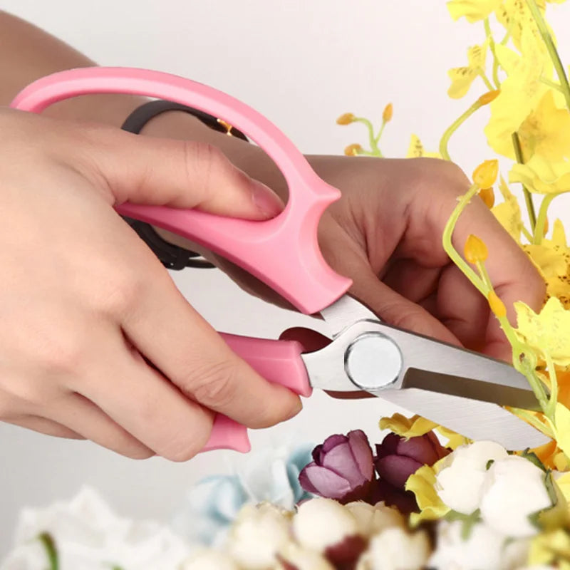 Hands holding pink precision bonsai and floral shears with comfort grips amidst yellow flowers