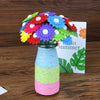 A bouquet of colorful felt flowers in various shades of red, purple, yellow, and blue displayed in a glass vase.