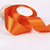 Orange satin ribbon rolled around a white candle with a natural stone in the background.