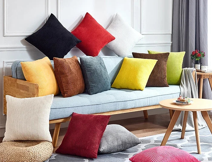 A collection of colorful velvet and corduroy cushion covers displayed on a light blue sofa.