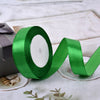 A roll of bright green satin ribbon is displayed on a white surface next to a small box and some decorative leaves.