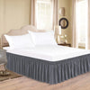A white bed with a thick gray ruffle skirt and adjustable elastic belt in a bedroom setting.