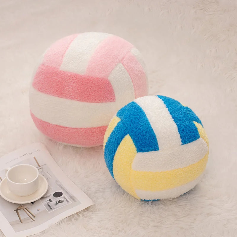 A pink and white striped plush volleyball ball resting on a white fuzzy surface next to a white cup and paper.