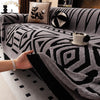A hand is touching a gray and black patterned knit sofa protector on a sofa.