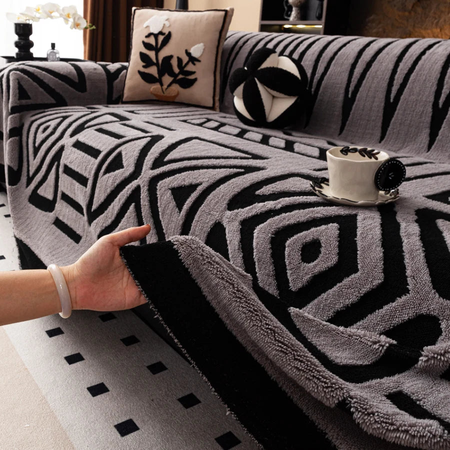 A hand is touching a gray and black patterned knit sofa protector on a sofa.