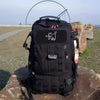 Black tactical backpack with an embroidered cute assassin cat patch resting on a rock.