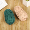 A ball of thick teal polyester craft yarn lying on a wooden surface next to a pale pink ball of the same yarn.