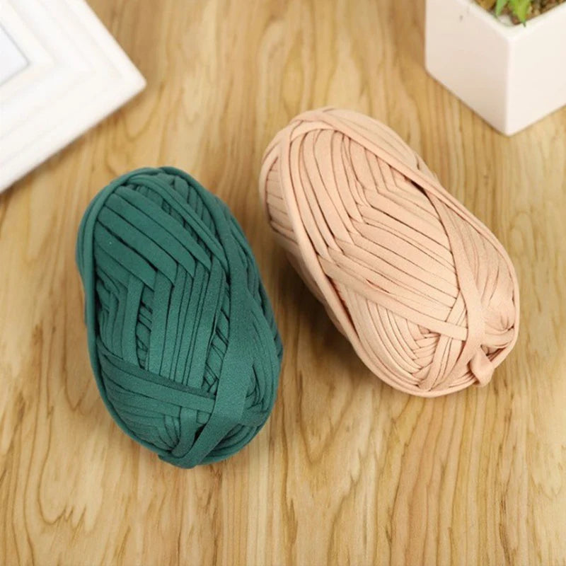 A ball of thick teal polyester craft yarn lying on a wooden surface next to a pale pink ball of the same yarn.
