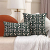 A set of dark green embroidered throw pillows resting on a white textured blanket next to a modern lamp.