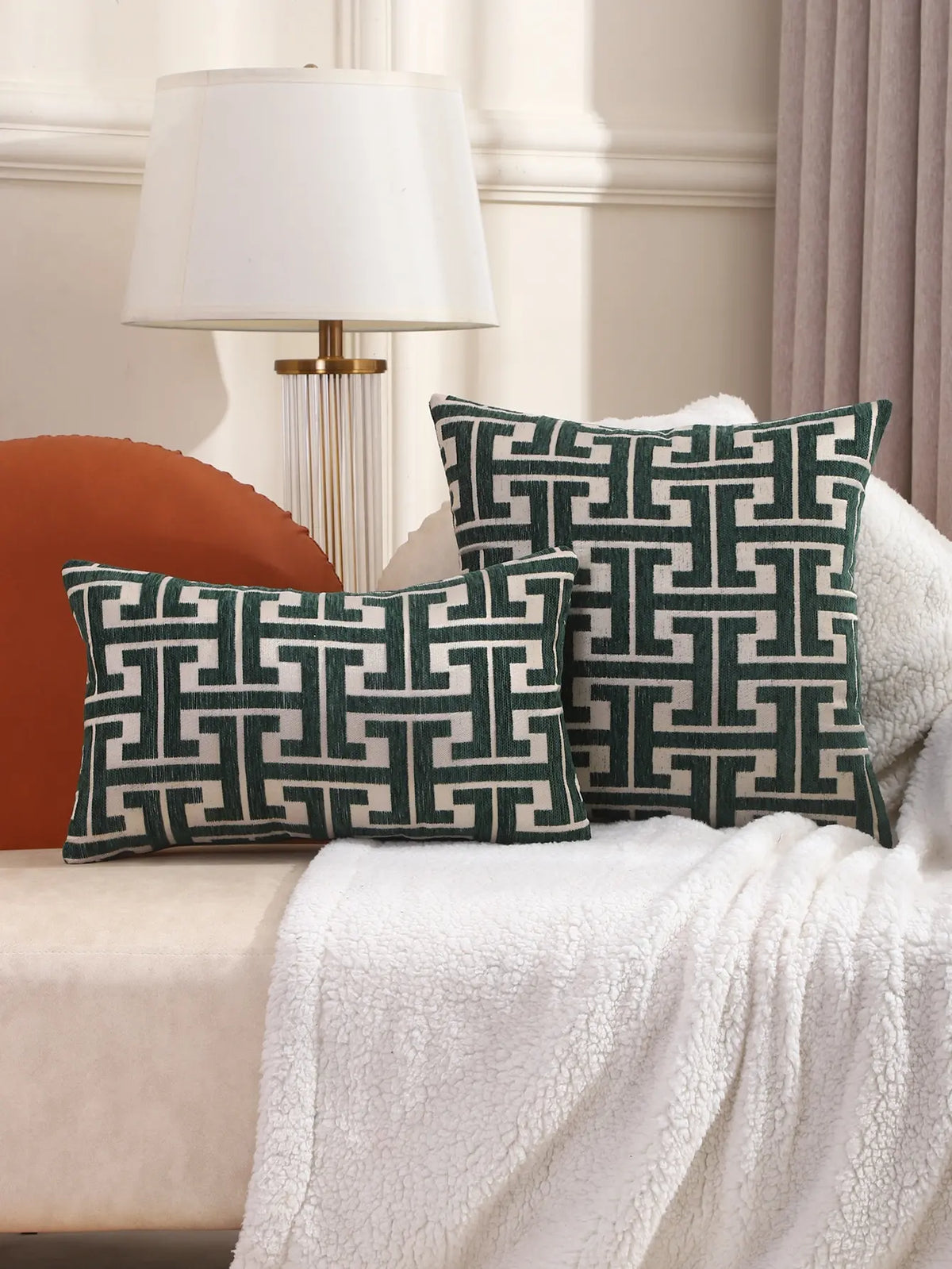 A set of dark green embroidered throw pillows resting on a white textured blanket next to a modern lamp.