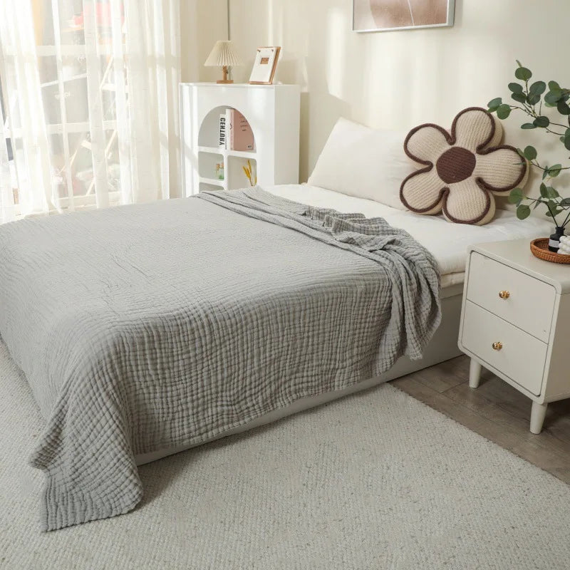 A light gray quilted blanket draped over a bed in a bright, minimalist bedroom setting.