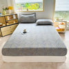 A fitted bed sheet with a gray and gold floral print is laid out on a bed in a bright room.
