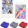A collection of hand-knitted yarn in purple, gray, and pink colors shown in close-up.