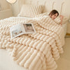 A thick, cream-colored, fluffy blanket is draped over a bed, with a person resting under it.