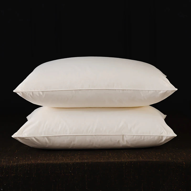 Two white natural goose down and feather sleeping pillows resting on a dark surface.