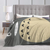 A Totoro character fleece throw blanket draped over a bed with white pillows and a gray headboard.