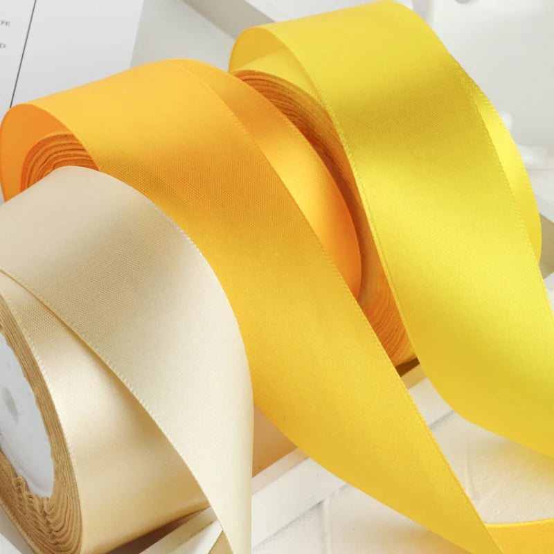 Rolls of satin craft ribbons in yellow and cream colors displayed on a white surface.