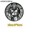 Black and white embroidery of a warrior figure wearing a helmet and armor on an oval patch.