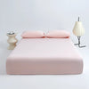 A set of pink ice silk cooling fitted bed sheets displayed on a white bed with two matching pillows.