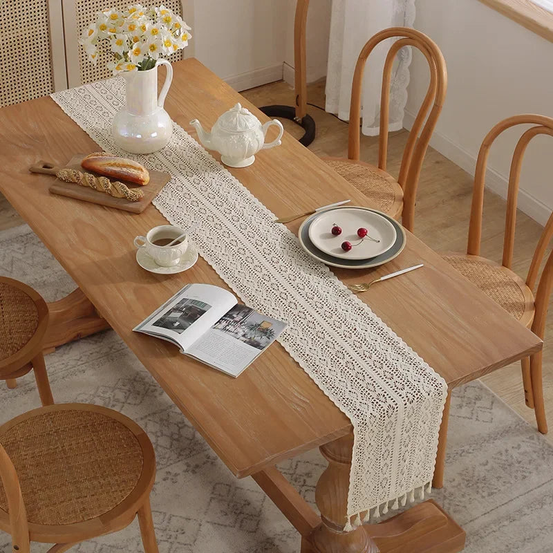 A wooden table is set with a vintage crochet lace table runner and various ceramic items.