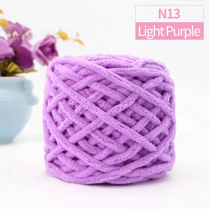 Purple chunky velvet knitting yarn in a skein with a blurred purple flower in the background.