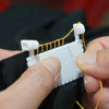 Hands are assembling a hinge-type fabric sewing guide with a measuring scale and yellow thread.