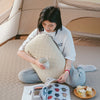 A person is reading a book while resting their head on a beige inflatable camping pillow in an outdoor tent setting.
