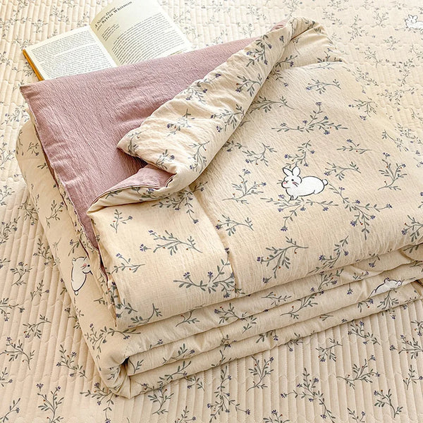 A stack of light beige cartoon quilting comforters and a book are displayed on a textured surface.