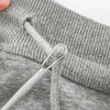 A close-up of a gray knitted garment showing a drawstring with a metal threader tool.