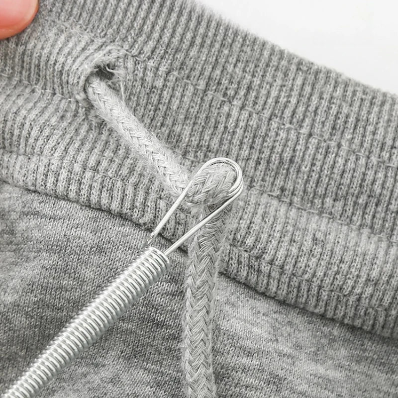 A close-up of a gray knitted garment showing a drawstring with a metal threader tool.
