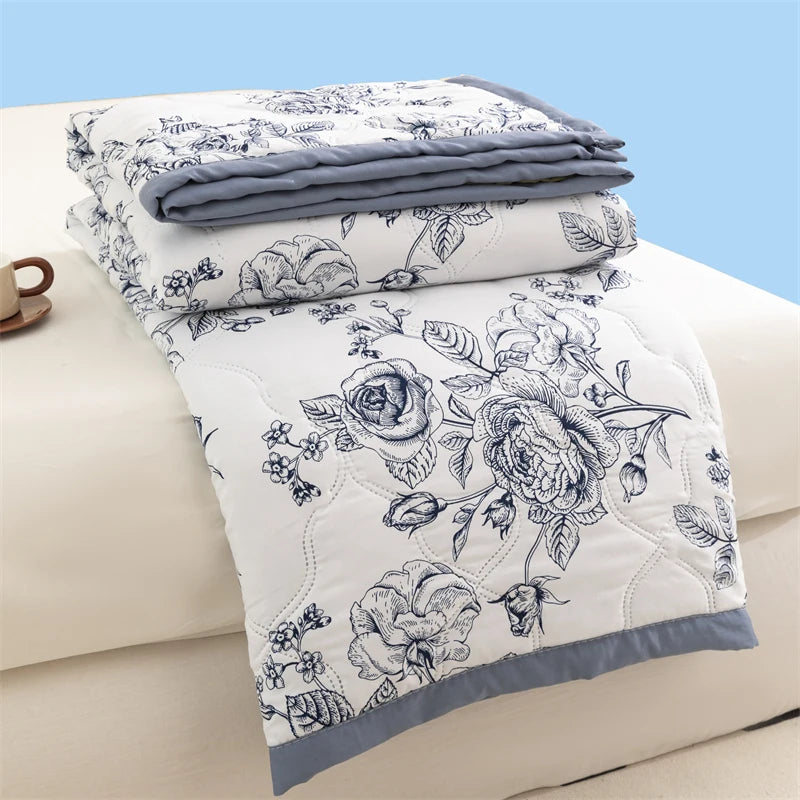 A white floral duvet cover and matching pillowcase set with gray accent trim, folded on a light beige bed.