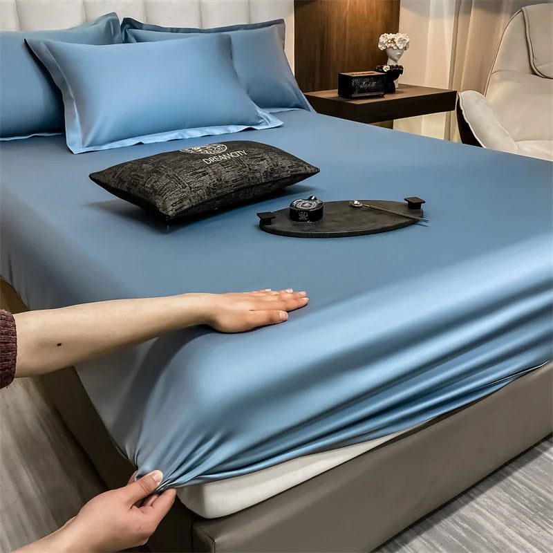 A light blue fitted bed sheet is draped over a bed, with a hand adjusting the fabric.