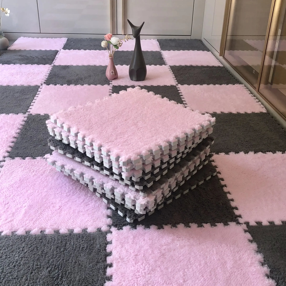 A pink and gray checkered rug mat with stacked white plush puzzle pieces and a black figurine on a floor.