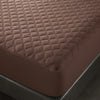 A close-up view of a brown quilted mattress protector on a dark bed frame.