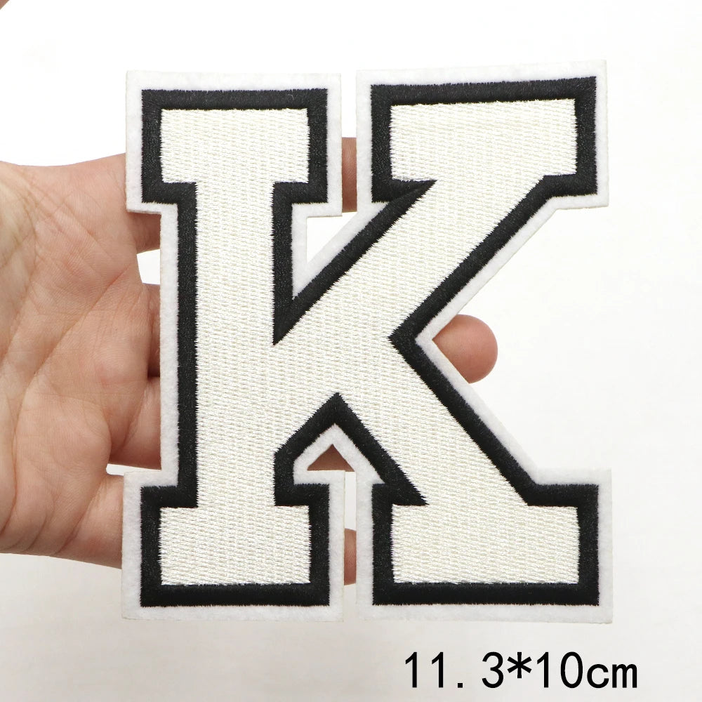 A hand holds a large black and white letter K patch for clothing decoration.