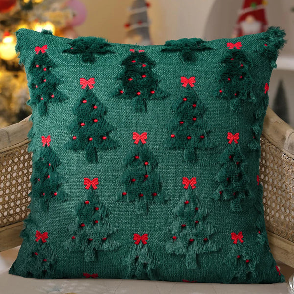 A deep green knitted cushion cover decorated with small red felt Christmas trees and bows.