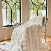 A white plush faux fur throw blanket draped over a metal hanger in front of a window.