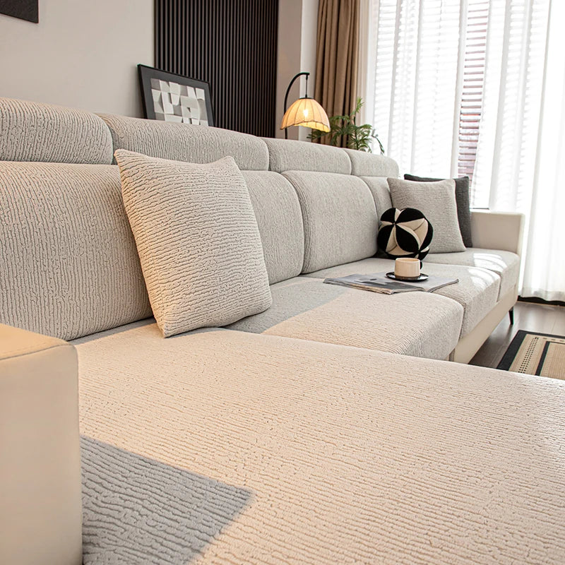 A light beige stretch sofa seat cushion cover on a modern sectional sofa with neutral decor.