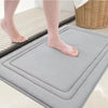 A gray ultra soft memory foam bathroom mat is placed on a tiled floor next to a person's bare foot.