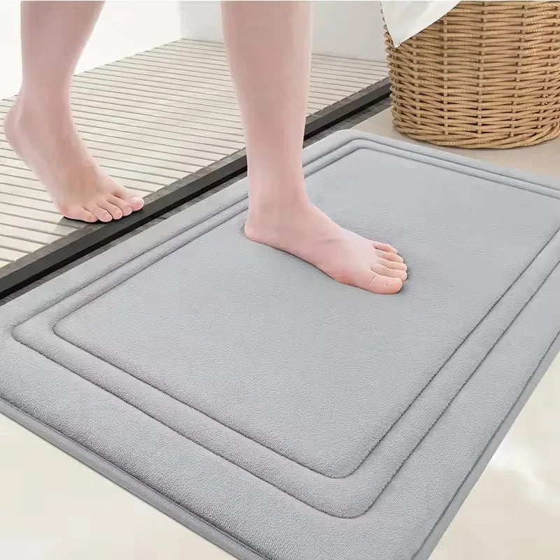 A gray ultra soft memory foam bathroom mat is placed on a tiled floor next to a person's bare foot.