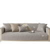 A light gray anti-slip sofa cover with several matching throw pillows on a couch.