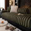 A dark olive green plush sofa seat cushion with vertical tufting rests on a black sofa, next to a white fluffy rug and brown 